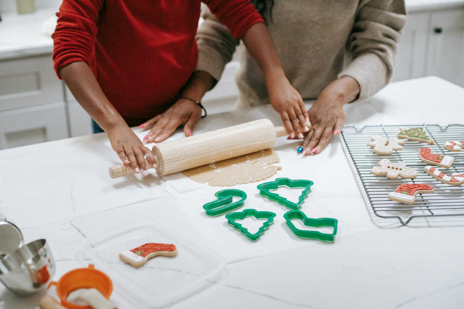 From above of crop unrecognizable ethnic child rolling out dough near parent while preparing gingerbread cookies in kitchen